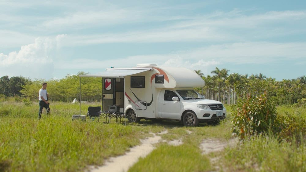 a man standing next to a camper in a field